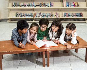 Five little childre sitting beside wood table,reading book and talking,doing activity together,happy moment at school,blurry light around