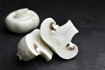 Fresh champignon mushrooms on dark background, sliced and whole, ready for cooking.
