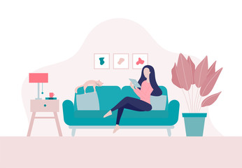 Stay home concept.Young woman sitting on a sofa at home with her cat and surfing on internet,shopping online using tablet in period of self isolation and social distancing during Covid-19 epidemic.