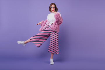 Surprised lovely girl in white shoes posing on purple background during indoor photoshoot....