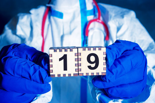 Scientist In Protective Suit Holds Two Wooden Cubes With The Number 19 In His Hands