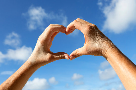 Close-up Of Woman Hand Holding Heart Shape On Beach Against Sky