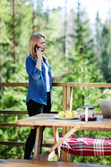 Displeased young woman talking on cell phone standing on wooden balcony of country house