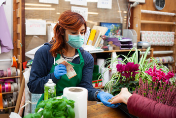 Florist in a nursery receives a payment from a customer wearing a mask and gloves due to the...