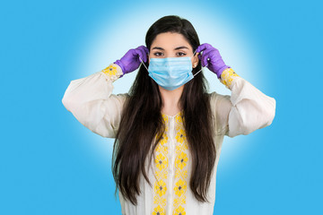 Young woman with protective surgical sterile gloves puts medical face mask. Protection against coronovirus, dust or pollen allergy, air pollution.  