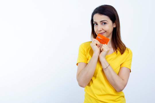 Giovane donna  con i capelli lisci, indossa una T-Shirt gialla e tiene in mano una carta di credito arancione con grande entusiasmo , isolata su sfondo bianco