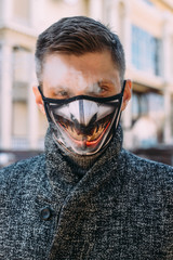 The guy on the street smokes an electronic cigarette and blows thick steam through the protective black  mask - 342416922