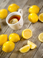 Cup of black tea with lemon slice and plenty of lemons around on grey wooden table. Warm drink infusion for cold fall and winter days. Concept of prevention for flu cold with Vitamin C