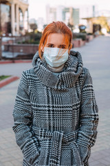 A beautiful red-haired woman in a medical mask for protection from coronavirus infection - 342416960
