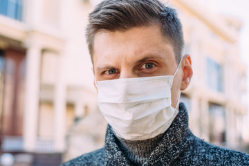 Close-up of an angry or surprised young man in a medical mask standing on the street and looking at the camera. Portrait of a guy who raised one eyebrow in surprise - 342417116