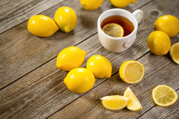 Cup of black tea with lemon slice and plenty of lemons around on grey wooden table. Warm drink infusion for cold fall and winter days. Concept of prevention for flu cold with Vitamin C