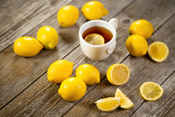 Cup of black tea with lemon slice and plenty of lemons around on grey wooden table. Warm drink infusion for cold fall and winter days. Concept of prevention for flu cold with Vitamin C