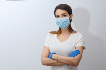 ragazza chiara con i capelli scuri raccolti indossa una mascherina di protezione e dei guanti blu, isolata su sfondo bianco