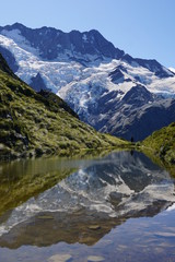 Naklejka na ściany i meble MOUNT COOK NATIONAL PARK, NEW ZEALAND - MARCH 12, 2020: Silhouette of a person reflecting in Sealy Tarns lake with glaciers in the background