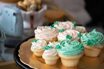 Close-up of bridal shower cupcakes on a gold tray with a blurred background of a camera and chocolates