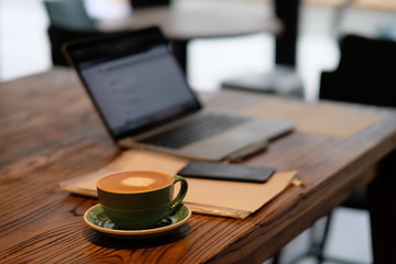 one cup of coffee and blurred laptop computer on wooden table, working in cafe concept. Blur background