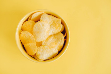 Potato chips in a yellow bowl on a yellow background. Top view. Copy, empty space for text