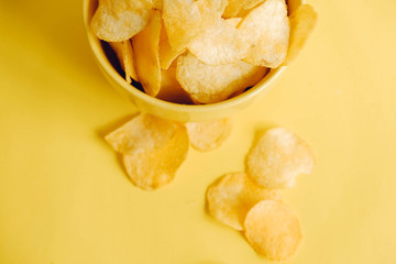 Potato chips in a yellow bowl on a yellow background. Top view. Copy, empty space for text