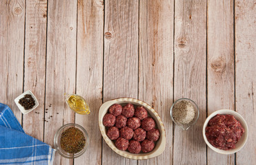 Obraz na płótnie Canvas Raw homemade beef meatballs, olive oil, salt and spices are ready to cook on a wooden background in the kitchen. Free space.