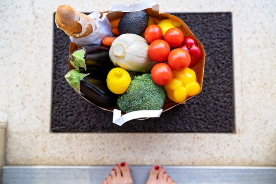 Contactless Food Delivery Service Concept. Top View At Bag With Grocery And Vegetables In Bag Delivered To Doorstep And Left. Online Shopping. Woman Picking Up Parcel At Entrance At Home.