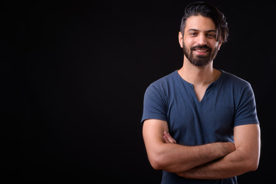 Portrait of happy handsome bearded Persian man smiling with arms crossed