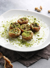 Eastern desserts. Vegan sweetness. Dried figs with walnuts and pistachio crumbs on a white plate on a light grey background with a fork. Menu restaurant. Background image, copy space