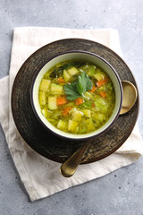 Lean vegetable soup with potatoes, zucchini, cabbage, carrots and herbs in a deep bowl with a spoon on a light grey background. Fresh parsley. Top view, flatlay. Background image, copy space