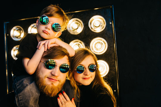 Rock Star Family. Stylish Family In Black Clothes And Glasses In The Light Of The Rays. Rock-n-roll Music Family Story