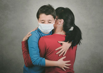 Sad child wearing medical mask hugging his mother