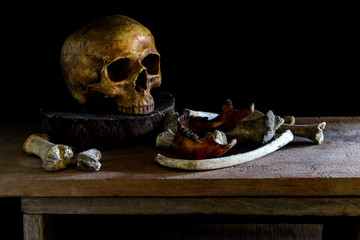 Human skulls and bones are placed on wood in a room with light shining on the side.