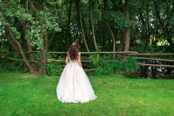 Beautiful bride stands with her back in a green meadow