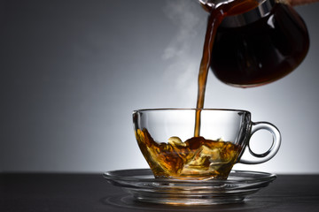 Pouring coffee with smoke on a transparent cup on black background