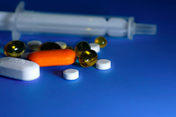 capsules, tablets and a syringe without a needle on a plain blue background. The concept COVID19