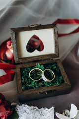 Wedding rings lie in a wooden box on a flower.