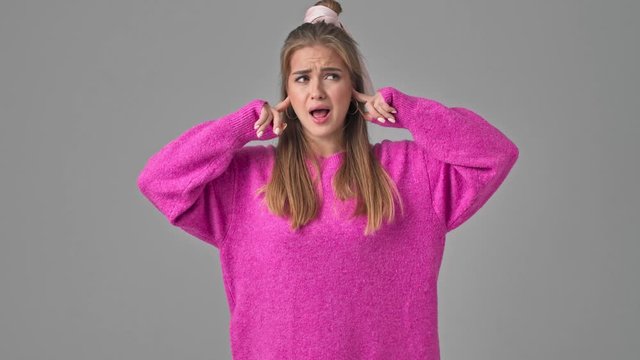 An attractive young woman is covering her ears while showing a nonsense content isolated over a grey background in studio