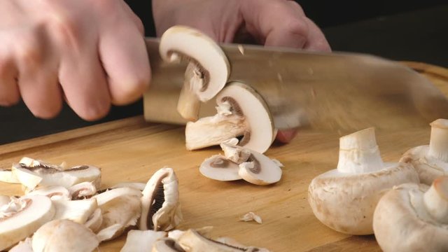 Hands of a woman cutting mushrooms on a wooden Board. Close up