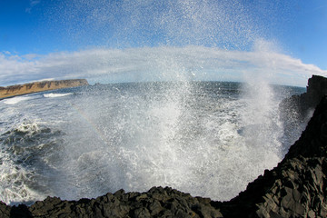 ocean wave crashing on coastal basalt rocks in Iceland. Sea spray