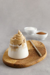 Korean drink. Homemade dalgona coffee in glass with milk on grey background. Trendy fluffy creamy whipped coffee.  Wooden stand.