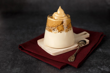 Homemade dalgona coffee in glass with milk on dark background. Trendy fluffy creamy whipped coffee on wooden stand. Korean drink.