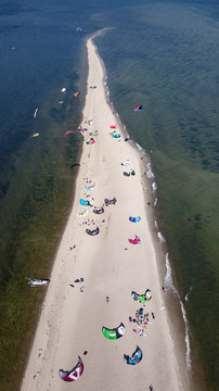 Aerial view of white sand beach peninsula with kites for kite surfing laying down on the beach and some kite surfers flying on the waves. Polish seaside coast with Baltic Sea's waters.