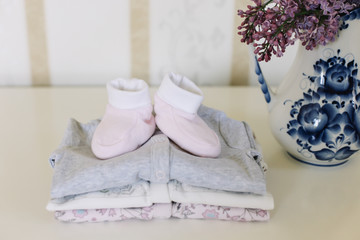 Beautiful pink baby clothes. Home cosiness. baby booties and clothes with a bouquet of flowers on the background. Newborn clothes