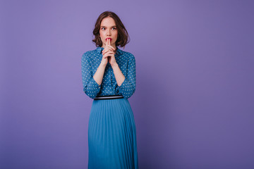 Good-looking pensive girl in long skirt looking away during photoshoot. Indoor portrait of concentraited brunette lady isolated on purple background.