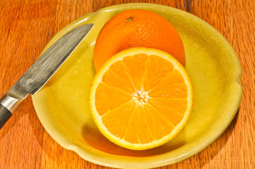 Top, front view, medium distance of, a freshly picked, Top view, very close distance, local, orange, cut in halve, view interior, a yellow-green plate,  a pairing knife, on a maple wood cutting board