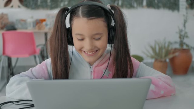 ni&ntilde;a con coletas en pijama de unicornio y auriculares conversa feliz en un port&aacute;til