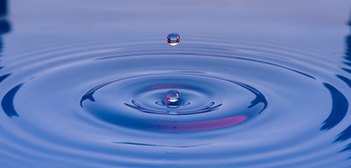 Gotas de agua color azul con morado suspendidas en el aire y  formando ondas en la superficie...