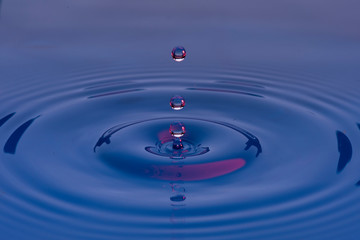 Gotas de agua color azul con morado suspendidas en el aire y  formando ondas en la superficie...