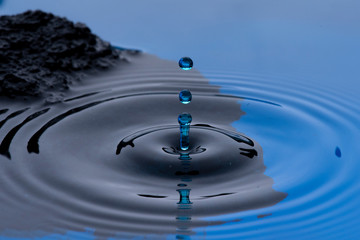 Gotas de agua color azul congeladas en el aire y formando ondas en la superficie liquida, con rocas...