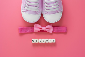 Baby girl pink background with newborn shoes, bow and Welcome words. Baby flat lay.