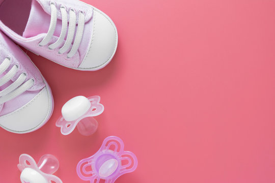 Baby girl background. Newborn shoes with pacifiers, pink background with copy space.