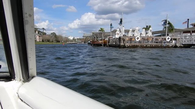 Driving In Water With Amphibious Vehicle Past Docking Port Structures And Buildings In Distance On Land 